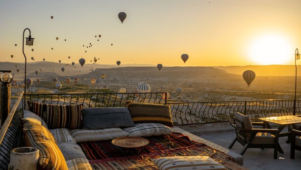 A terrace with a sofa and chairs, overlooking a landscape with hot air balloons. - Ages in Cappadocia (Nevsehir)