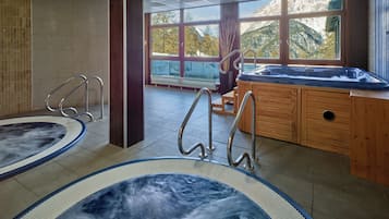 Un área de spa con dos jacuzzis, armarios de madera y vistas a montañas a través de amplios ventanales.