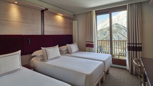 A hotel room with two beds, a large window with curtains, and a view of snow-covered mountains. - Hotel Sansicario Majestic (Cesana Torinese)
