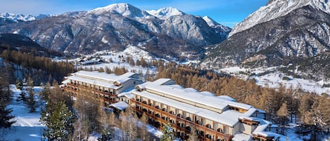 Un hotel de varios pisos, con un paisaje nevado y montañas al fondo.