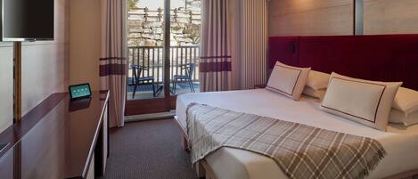 A hotel room with a bed, a TV, a desk, and a balcony with a view of the outside.
