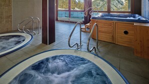 A spa area with two hot tubs, wooden cabinets, and a view of mountains through large windows. - Hotel Sansicario Majestic (Cesana Torinese)