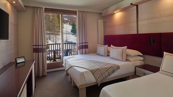 Hotelkamer met een groot bed, een bureau, een televisie en een balkon met uitzicht op bomen en sneeuw.