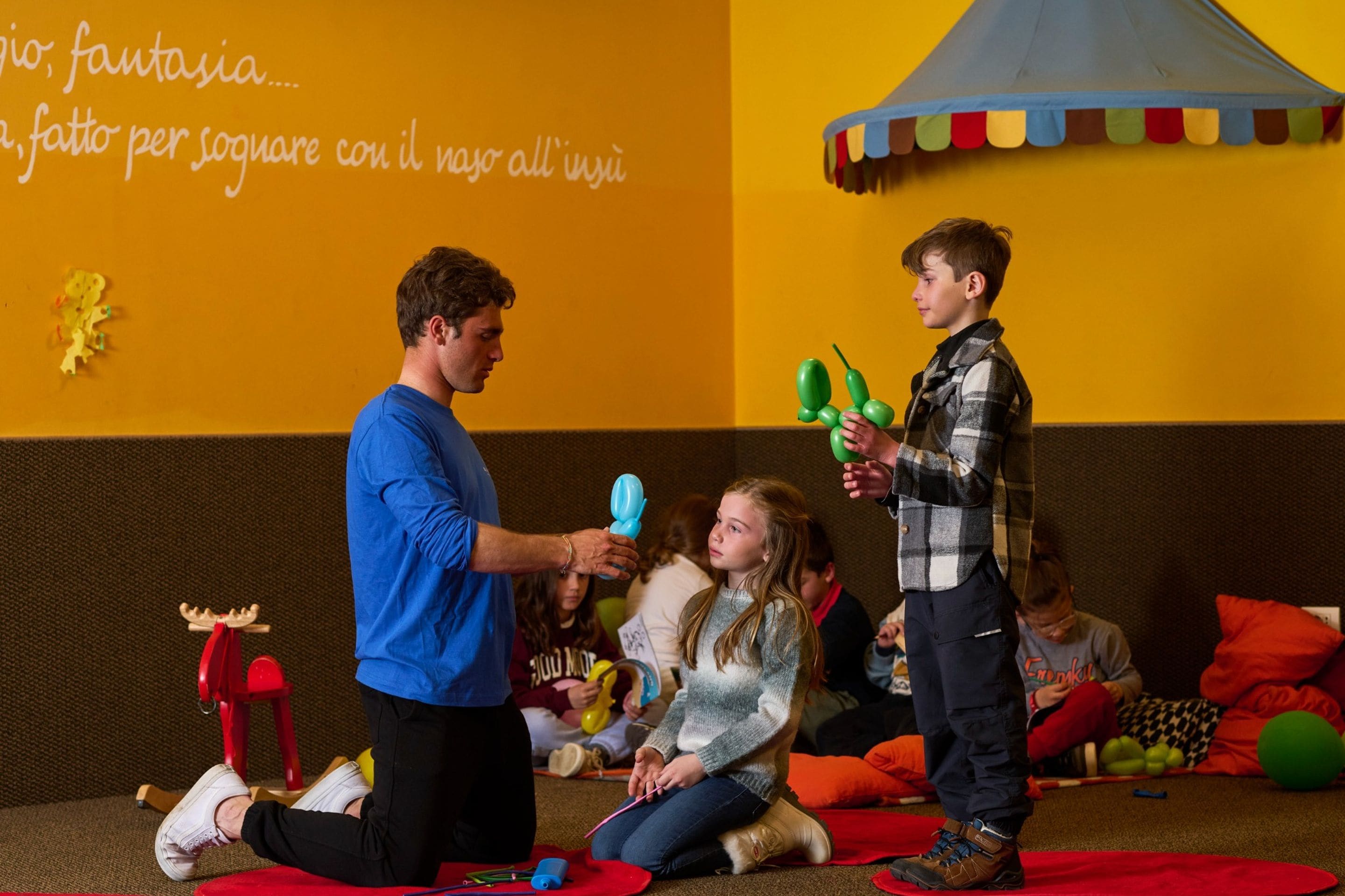 A group of people engaged in an activity with balloons and a wall with text in a room with a yellow wall and a red carpet.
