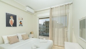 Un dormitorio moderno con una cama grande, una mesita de noche, una ventana con cortinas translúcidas y vistas a edificios.