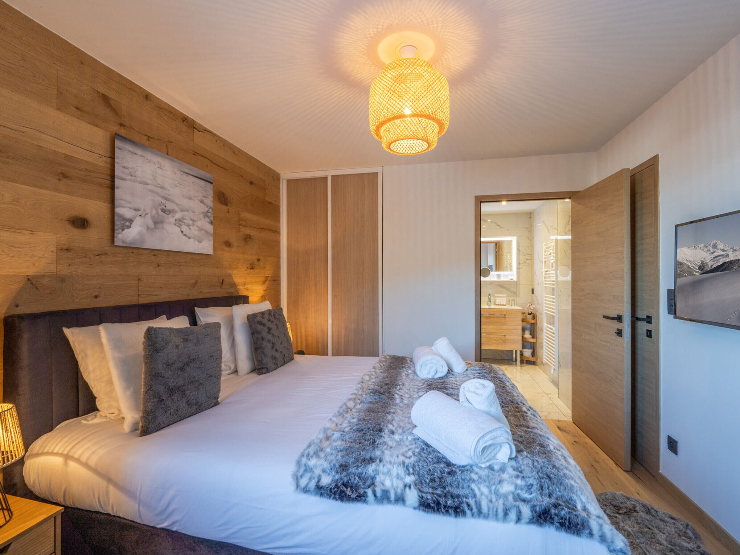 A modern bedroom with a wooden headboard, a large bed with white linens, a fluffy rug, and a ceiling light fixture.