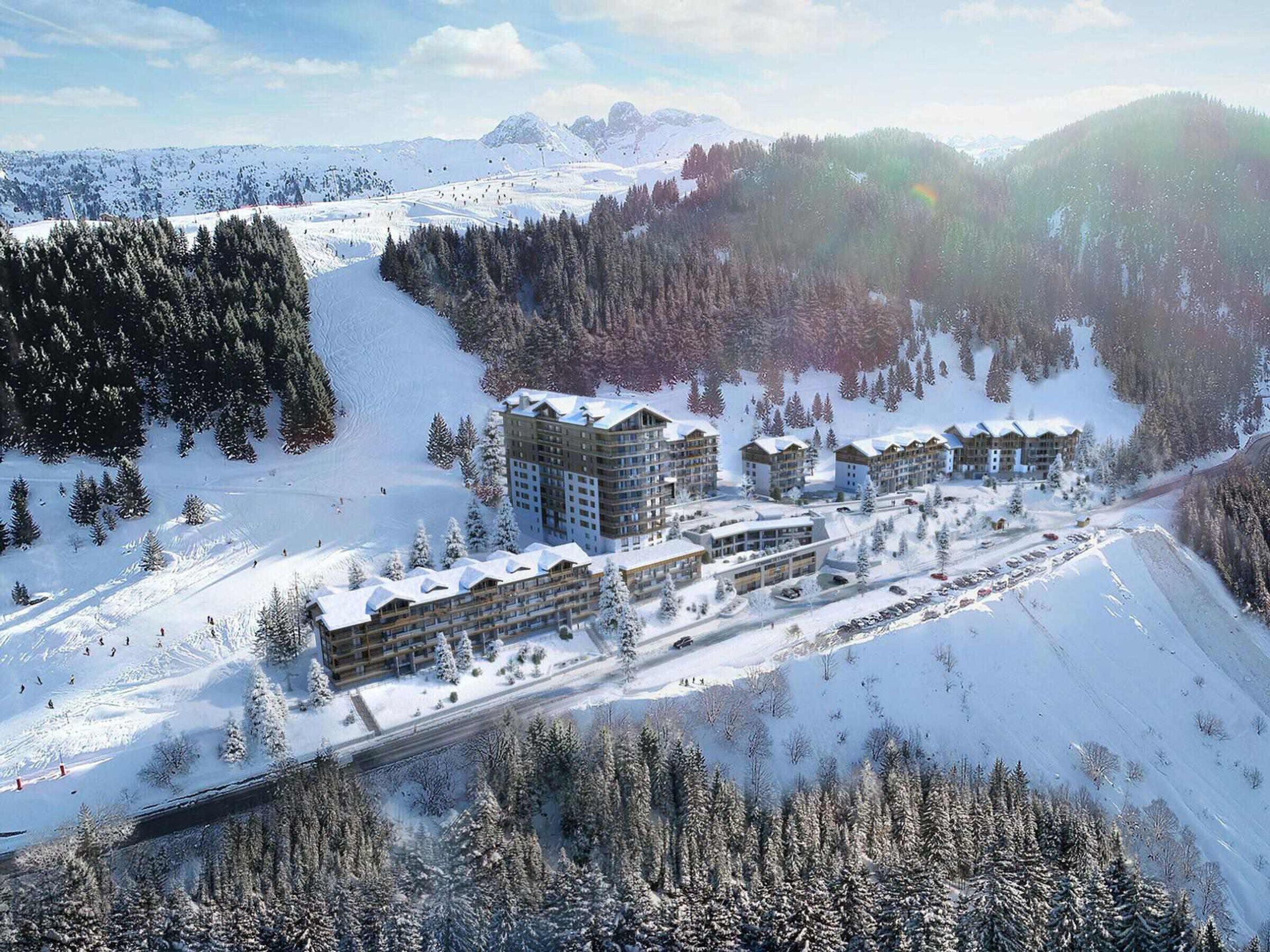 Un centro turístico en la montaña cubierto de nieve, con varios edificios, pistas de esquí y un bosque denso.