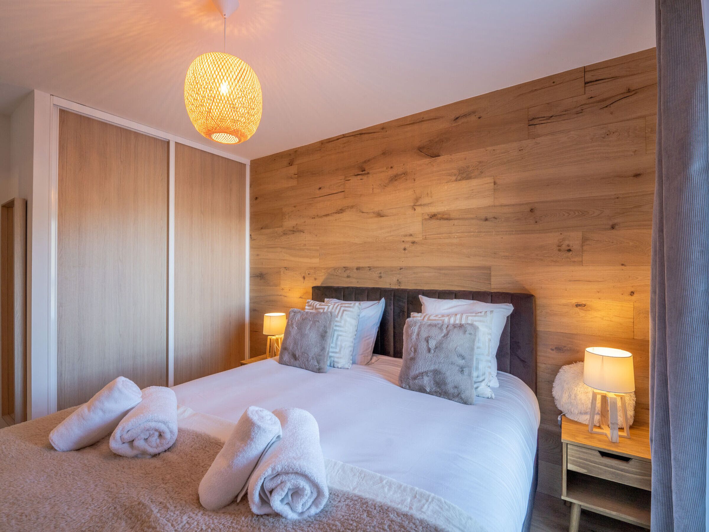 Ein Schlafzimmer mit einem hölzernen Kopfteil, einem großen Bett mit weißer Bettwäsche, zwei Nachttischlampen und einer Pendelleuchte.