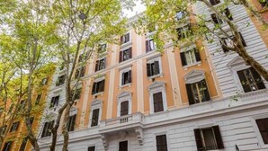 Un immeuble à plusieurs étages de style architectural classique, caractérisé par des fenêtres disposées de manière symétrique et une entrée centrale surmontée d’un balcon.