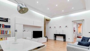 Un salon moderne comprenant un coin repas, des meubles blancs, un téléviseur à écran plat et une cheminée.