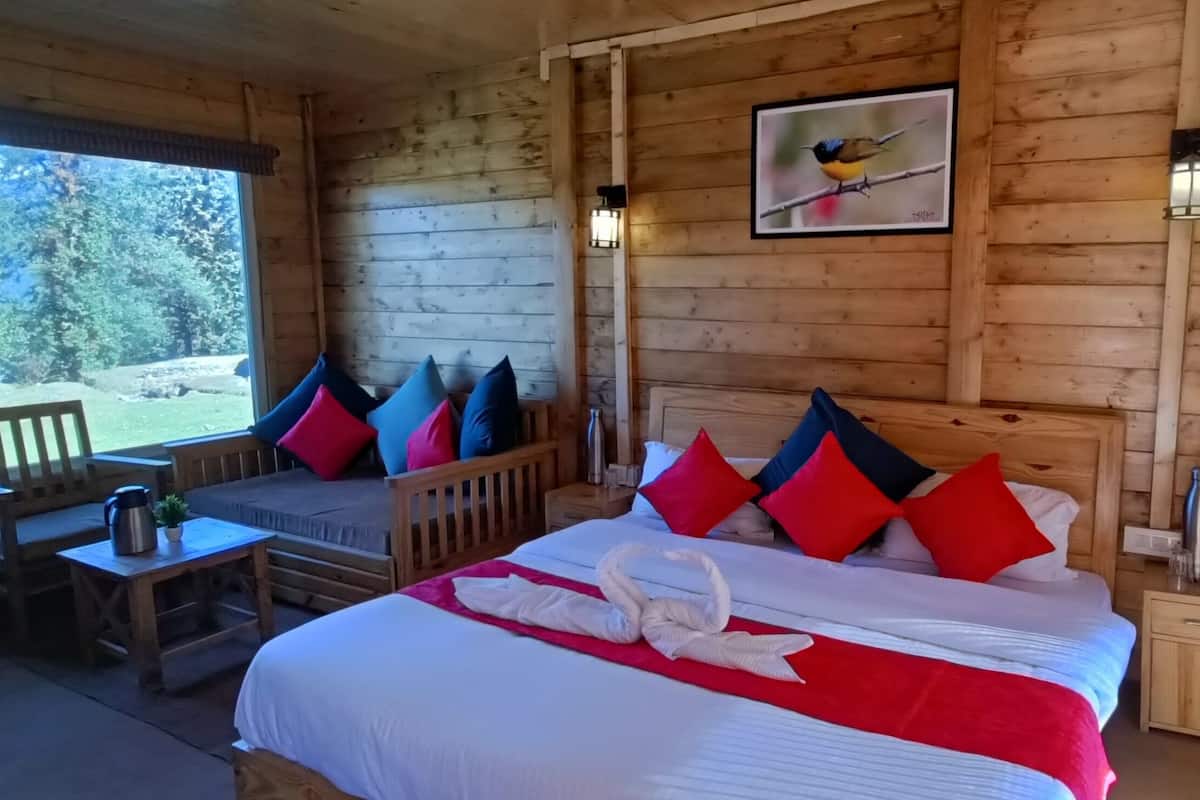 A wooden cabin room with a bed, pillows, a window, a table, and a chair.