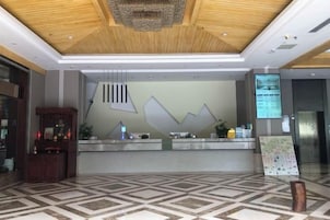 A hotel reception area with a modern design, featuring a reception desk, a digital screen, and a patterned floor.