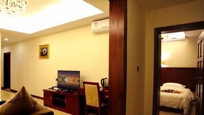 A hotel room with a bed, a desk with a television, a chair, and a wall-mounted air conditioner.