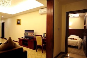 Ein Hotelzimmer mit Bett, Schreibtisch mit Fernseher, Stuhl und Wandklimaanlage.