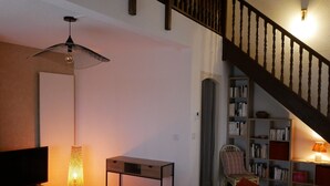 Una sala de estar con televisión, una mesa, un sofá, una estantería y una escalera.