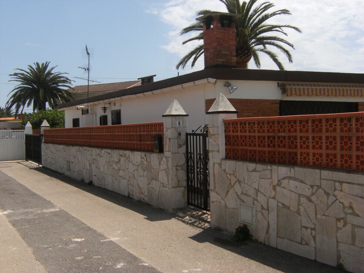 A building with a stone facade, a metal gate, and a palm tree in the background.