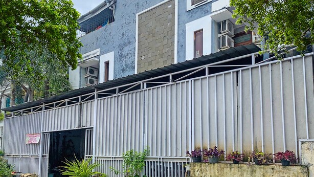 A building with a corrugated metal fence, a brick wall, and a window with a metal shutter.