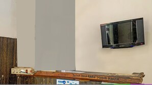 A television mounted on a wall, a wooden beam, and a sign with text.