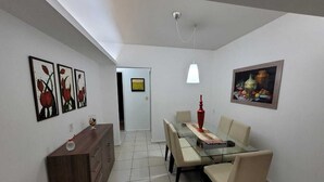 Un comedor con mesa de vidrio, sillas color beige, un armario de madera y obras de arte en las paredes.