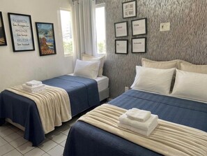 A hotel room with two beds, a window with curtains, and wall art.