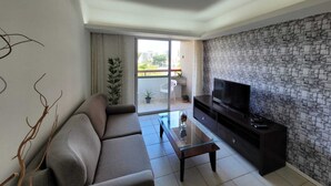 Una sala de estar moderna con un sofá, una mesa de centro de vidrio, un televisor sobre un mueble negro y una pared con diseño de piedra.