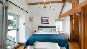 A bedroom with a bed, a chandelier, a window, and wooden beams. - Long Roods Cottage, Monsal Head, near Bakewell (Bakewell)