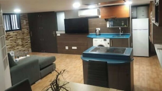 Cocina compacta con estufa integrada, lavaplatos y refrigerador. Hay una zona de comedor con una mesa y sillas.
