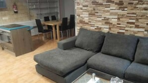 Una sala de estar moderna con un sofá seccional gris, una mesa de centro de vidrio y una cocina al fondo.