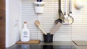 Eine Küche mit einer weißen Flasche mit dem Aufdruck 'olio', einem schwarzen gewebten Behälter für Holzbesteck und Edelstahlküchenutensilien, die an der Wand hängen.