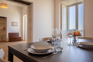 A dining area with a table set for two, a window with a view, and a bookshelf in the background.