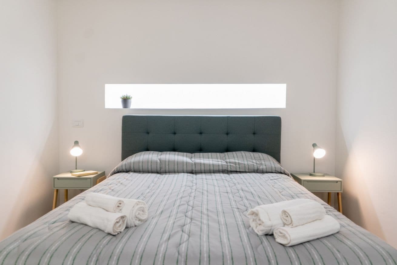 A neatly made bed with striped bedding, two bedside lamps, and a small potted plant on the wall.