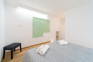 A bedroom with a bed, a bench, a green wardrobe, and a light fixture. - GuestHost - Modern 120 sqm apartment with sea view, finely furnished, for up to 4 people, located on the ground floor of a building (a few steps to access it). The accommodation is located in the heart of Ortigia, the marvelous historic center of Syracus (Siracusa)