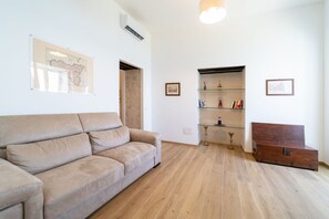 A living room with a beige sofa, a wooden floor, a glass cabinet with decorative items, and a wooden chest. - GuestHost - Modern 120 sqm apartment with sea view, finely furnished, for up to 4 people, located on the ground floor of a building (a few steps to access it). The accommodation is located in the heart of Ortigia, the marvelous historic center of Syracus (Siracusa)