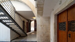 Um corredor com escadas, uma porta de madeira com placa de identificação e um pilar de pedra.