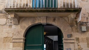 Um edifício de pedra com uma porta verde, varanda com grades brancas e uma placa com número.