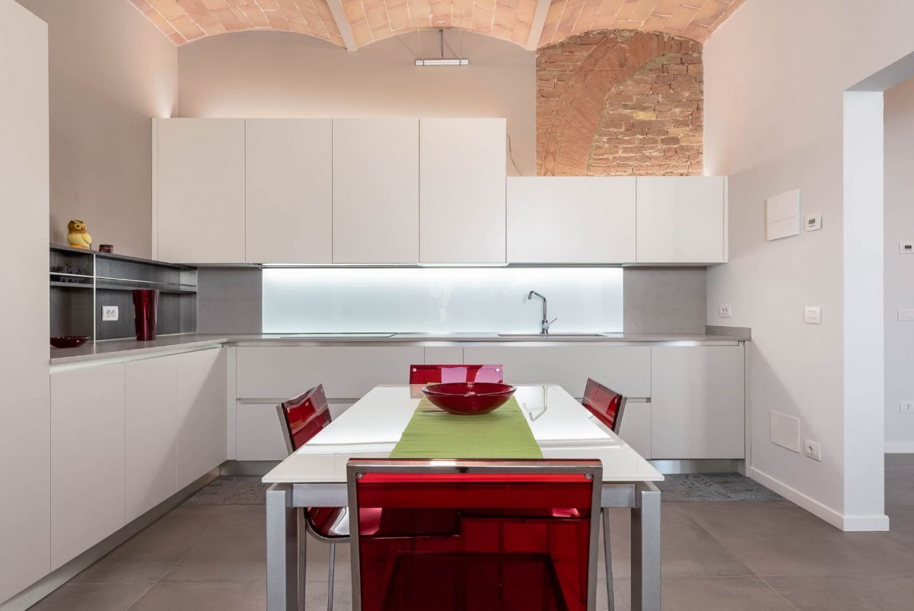 Una cucina moderna con mobili bianchi, una ciotola rossa sul tavolo e una parete in mattoni.