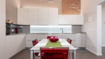 Una cucina moderna con mobili bianchi, una ciotola rossa sul tavolo e una parete in mattoni.