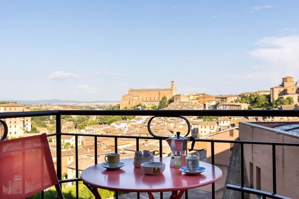 A balcony with a table set for tea, overlooking a historic cityscape with buildings and a prominent tower. - GuestHost - Siena Historic Center Stylish Flat with Balcony! (Siena)