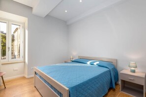 A bedroom with a bed, bedside tables, a window, and a view of buildings outside. - GuestHost - Siena Historic Center Stylish Flat with Balcony! (Siena)