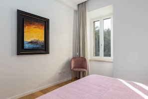 Una habitación con una cama, una silla, un ventanal y un cuadro en la pared.