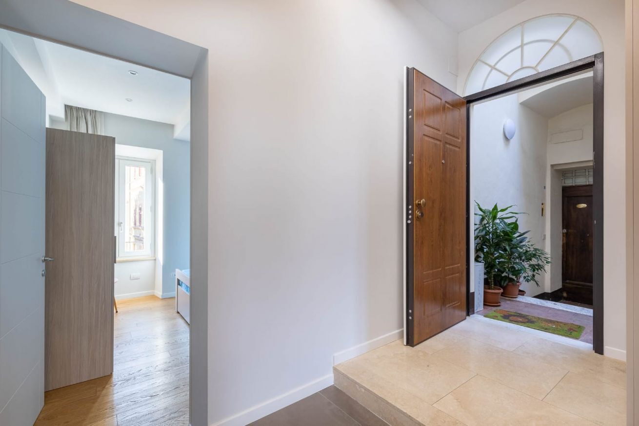 Un corridoio con una porta in legno, una pianta in vaso e vista su un'altra stanza.