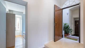Un corridoio con una porta in legno, una pianta in vaso e vista su un'altra stanza.