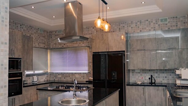 A modern kitchen with a central island, stainless steel appliances, and a large window with blinds. - Pomona BB House in Pomona Harare 7 Suites Executive &  Group Options  Best Value (Harare Harare)