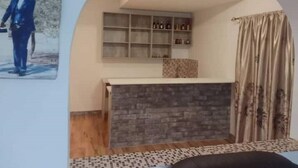 A room with a stone fireplace, a built-in shelf with bottles, a patterned rug, and a framed picture on the wall. - Pomona BB House in Pomona Harare 7 Suites Executive &  Group Options  Best Value (Harare Harare)