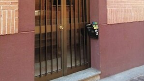Une entrée d’immeuble avec un portail en métal, une boîte aux lettres et une petite marche menant à la porte.