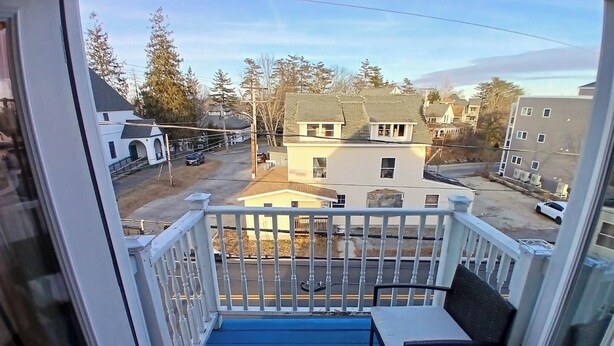 A balcony with a blue floor, white railing, and a single black chair. - A bedroom balcony with a view to the Ocean.  7 min walk to the beach (Old Orchard Beach)