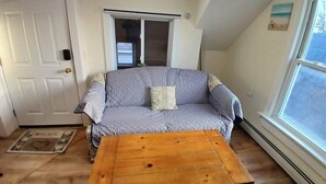 A room with a striped sofa, a wooden table, a door, and a window. - A bedroom balcony with a view to the Ocean.  7 min walk to the beach (Old Orchard Beach)