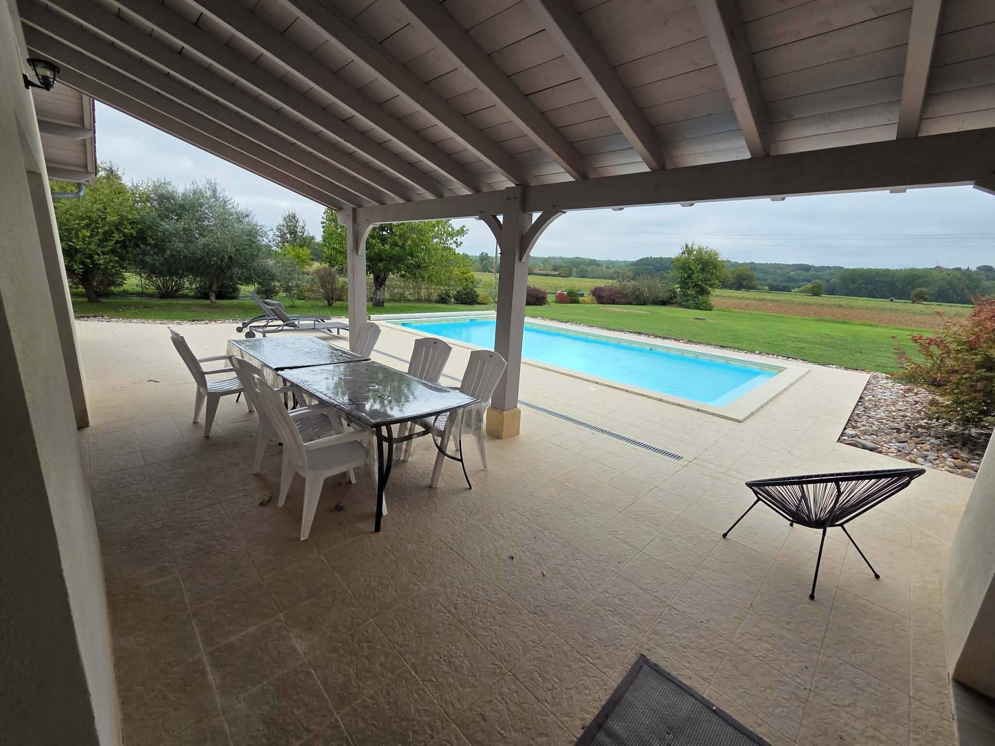 Un patio couvert avec une piscine, du mobilier d’extérieur et une vue sur le paysage environnant.