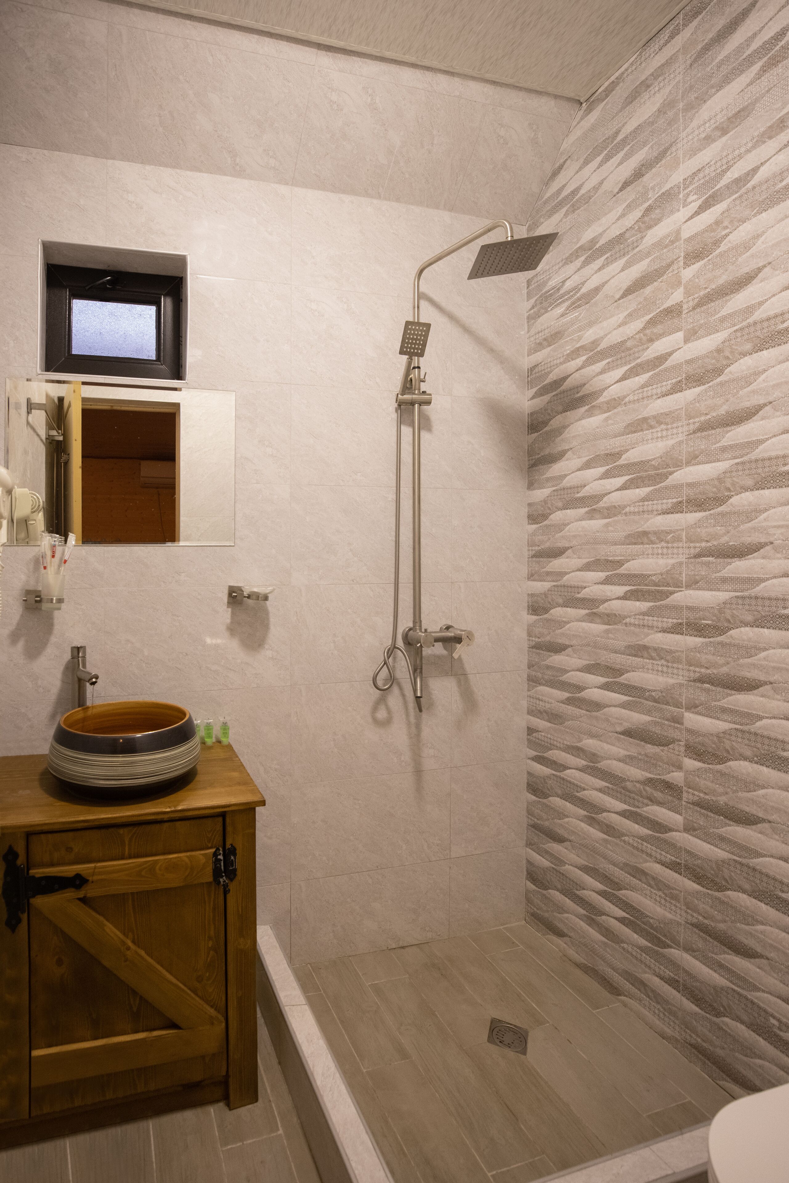 A bathroom with a wooden vanity, a built-in sink, a shower with a handheld showerhead, and a patterned wall.