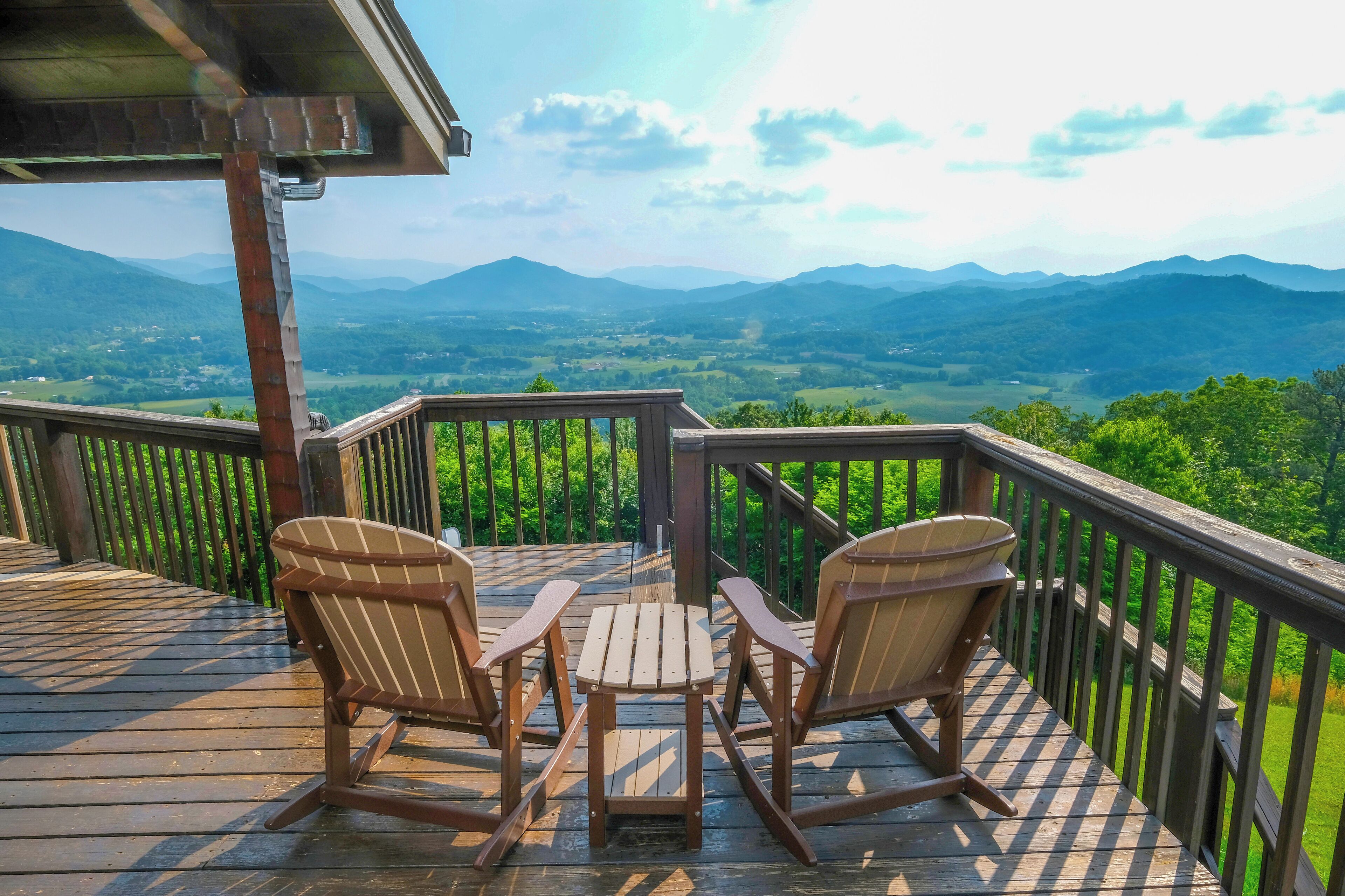 Une terrasse en bois avec deux fauteuils Adirondack et une petite table, offrant une vue imprenable sur un paysage montagneux.